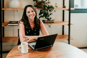 Emily Hockstra smiles in front of her laptop with a coffee mug.